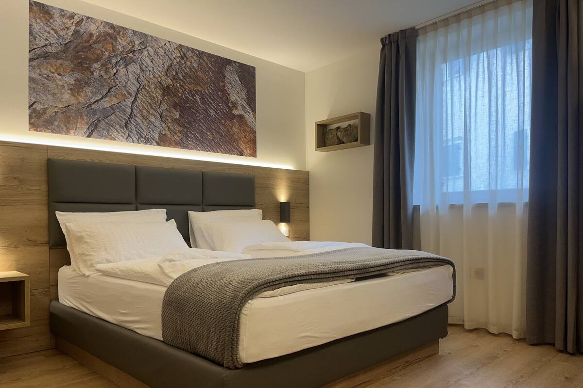 A modern bedroom with a large bed, wooden headboard, and a large abstract painting above it.
