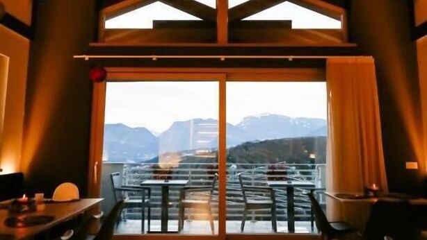 A dining area with a high ceiling and large windows overlooking a mountainous landscape. - Le Rocce Val di Non - Quality Room & Breakfast  (Ville d'Anaunia)
