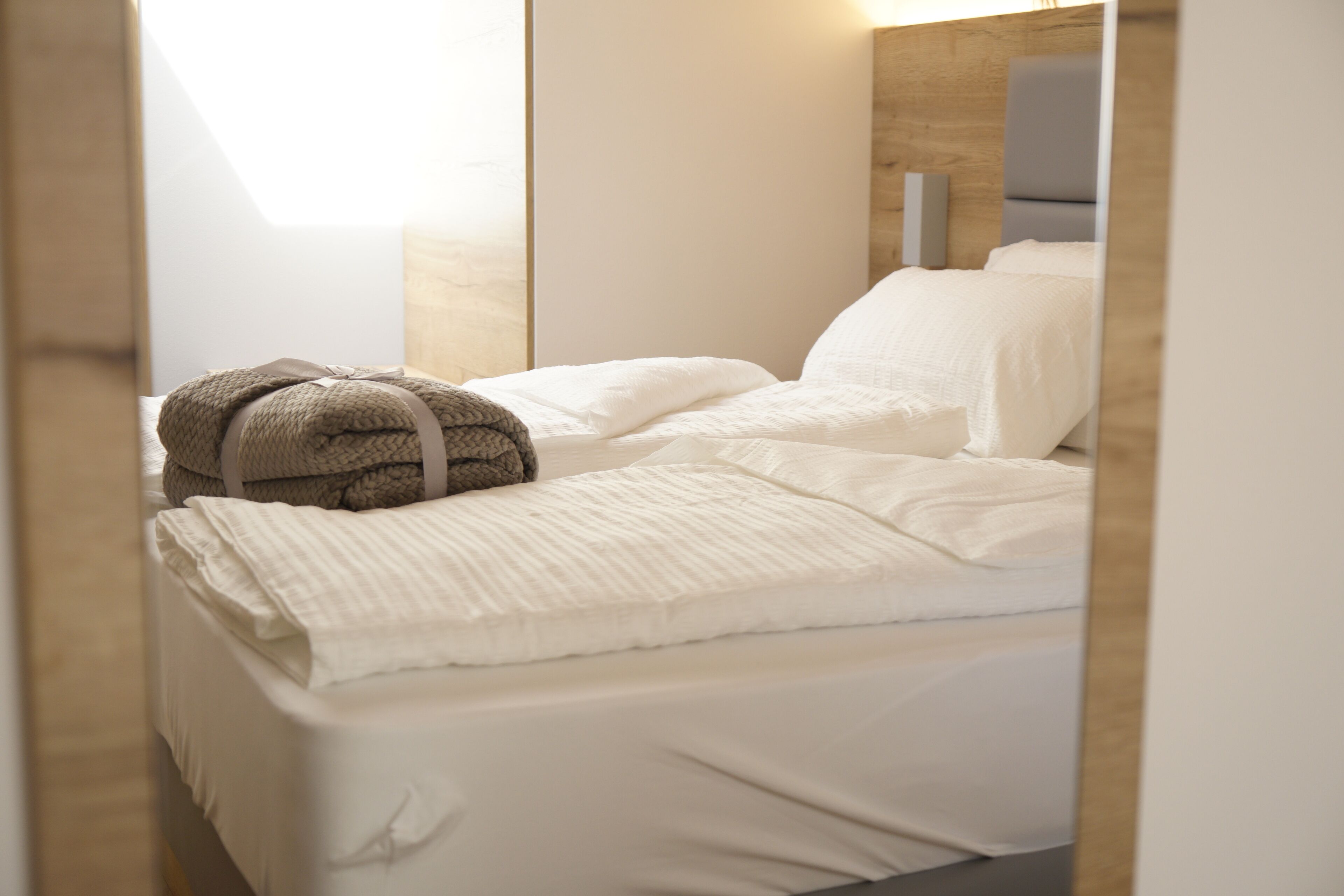 A neatly made bed with white linens and a brown towel, a wooden headboard, and a bedside table with a lamp.