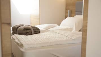 A neatly made bed with white linens and a brown towel, a wooden headboard, and a bedside table with a lamp.