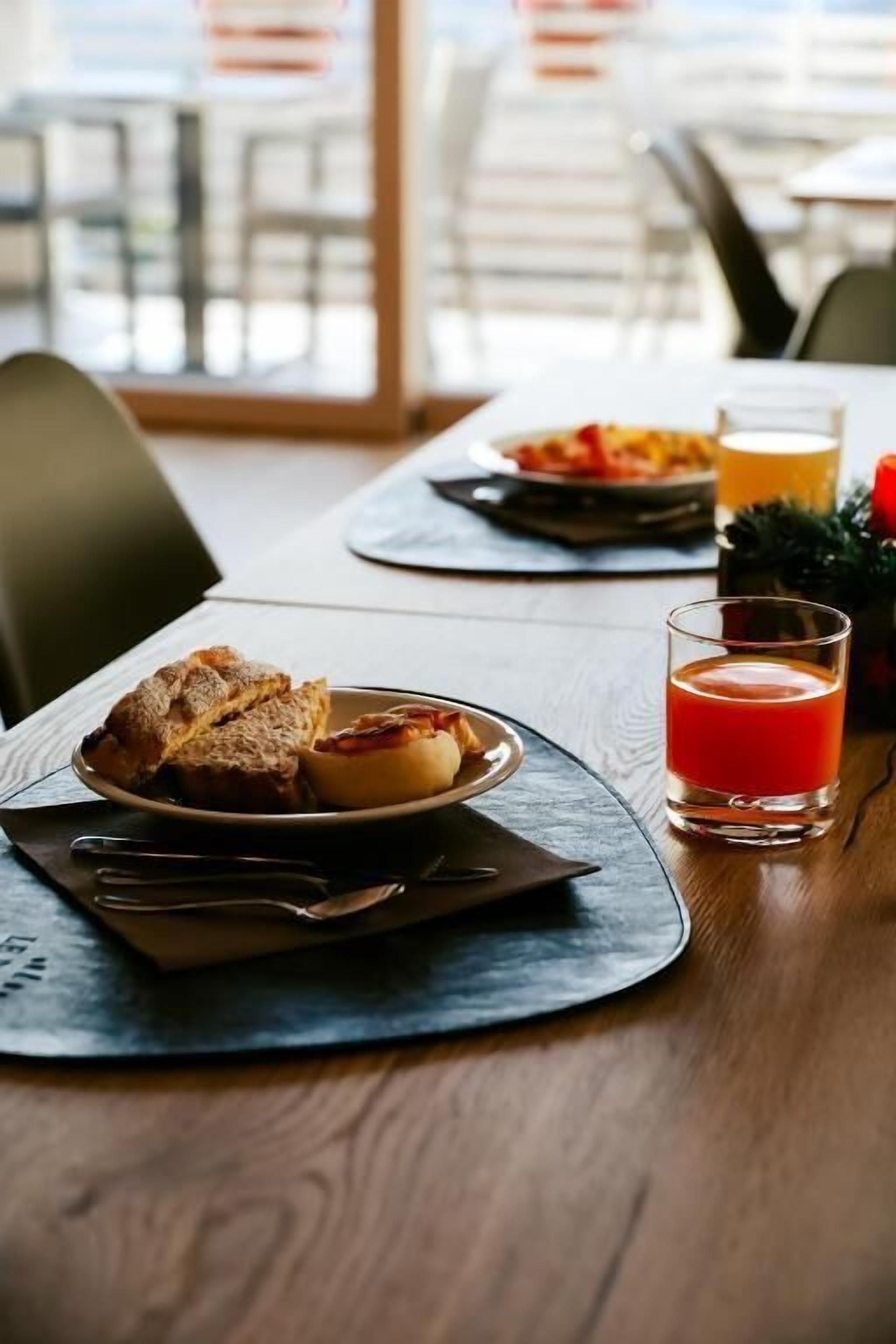 Aamiaispöytä, jossa on lautasellinen leivonnaisia ja lasi appelsiinimehua puupöydällä.