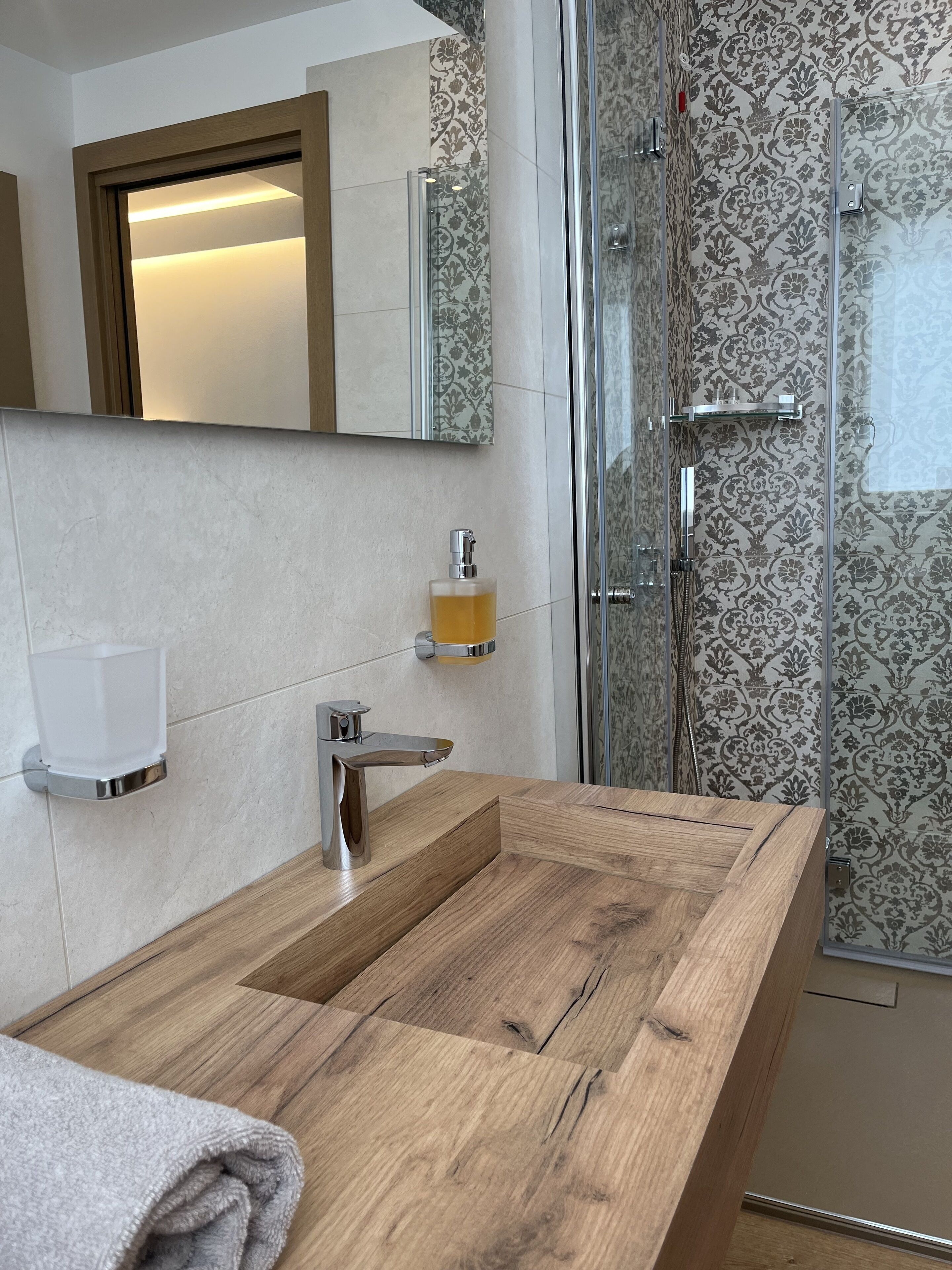 Une salle de bain moderne avec un meuble-lavabo en bois, une cabine de douche en verre et un papier peint à motifs.