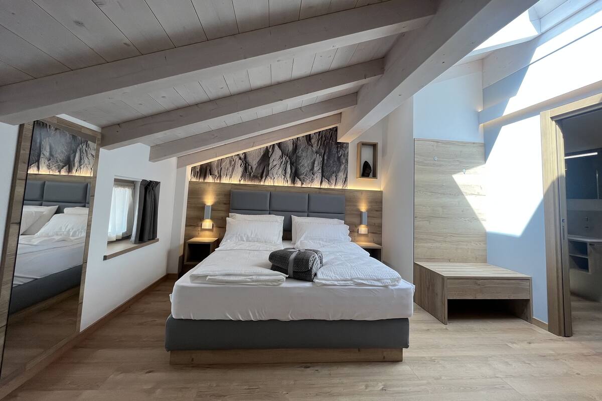 A modern bedroom with a large bed, wooden ceiling beams, and a skylight.