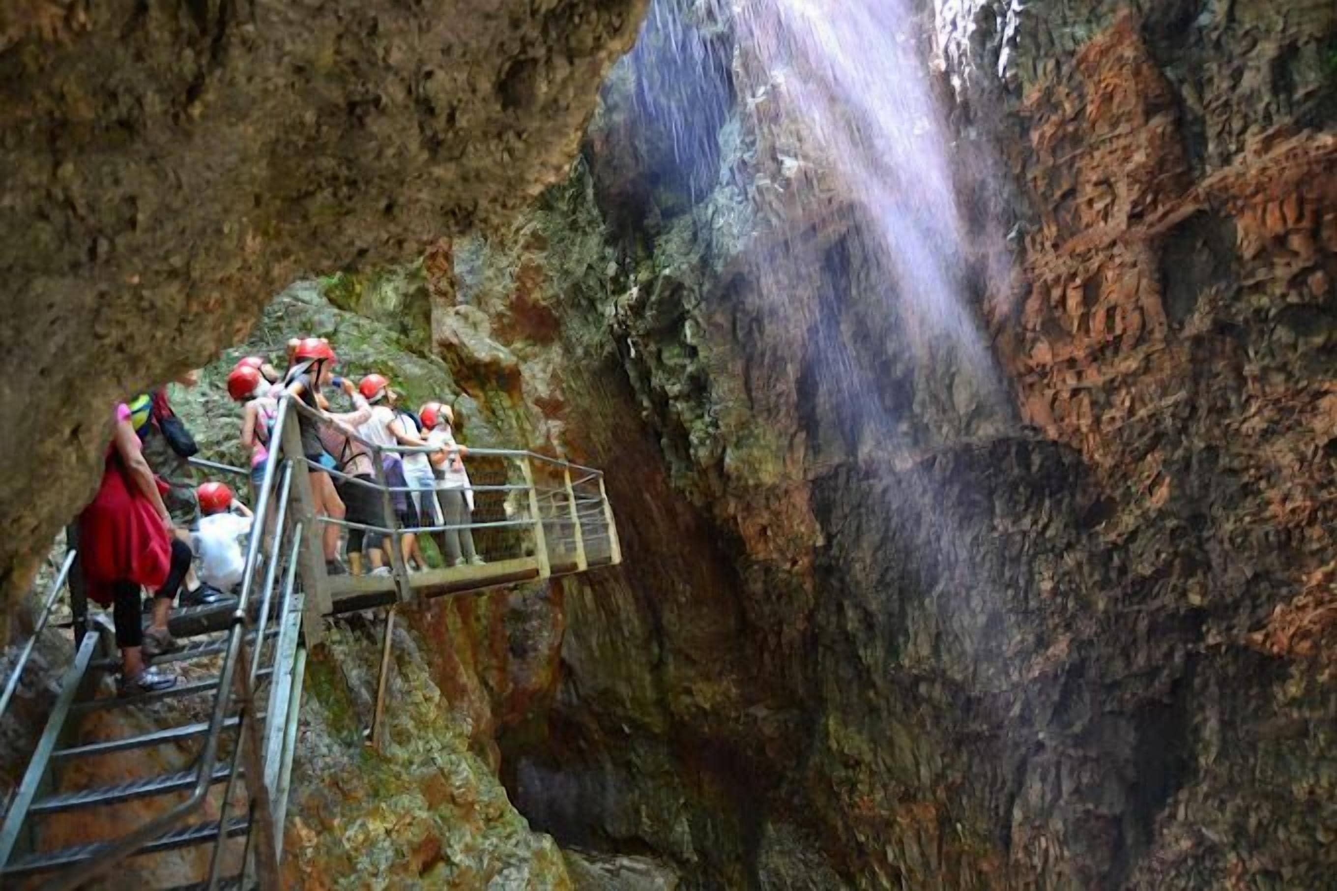 Un grupo de personas en una plataforma metálica con barandillas, contemplando una cascada en un cañón rocoso.