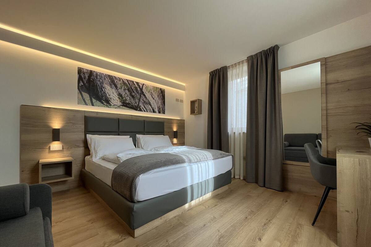 A modern hotel bedroom with a large bed, bedside tables, a desk, and a chair.