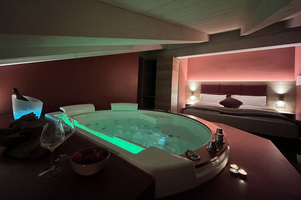 A modern spa room with a hot tub, a glass of wine, and a bowl of strawberries.
