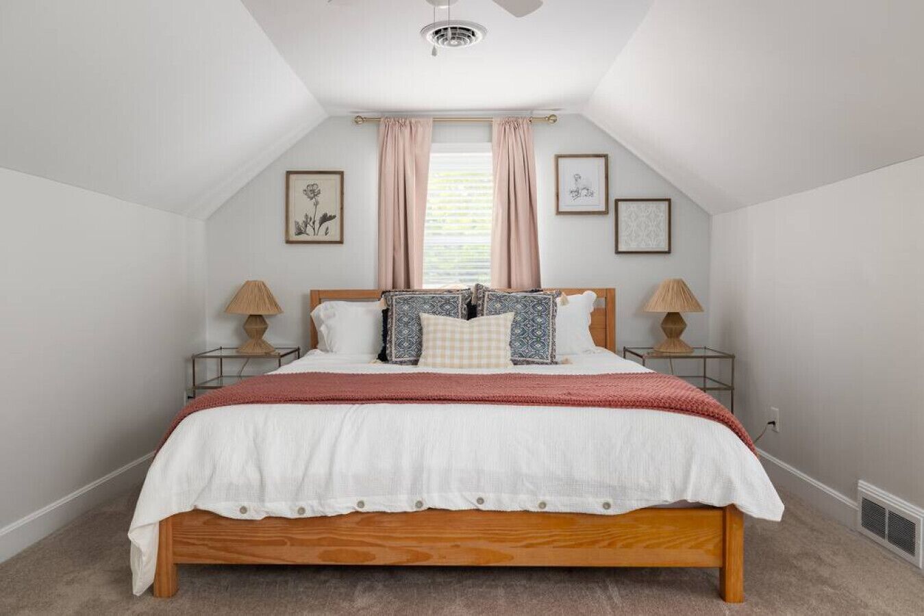 Une chambre à coucher avec un lit en bois, deux tables de chevet avec des lampes, une fenêtre avec des rideaux et des tableaux encadrés accrochés au mur.