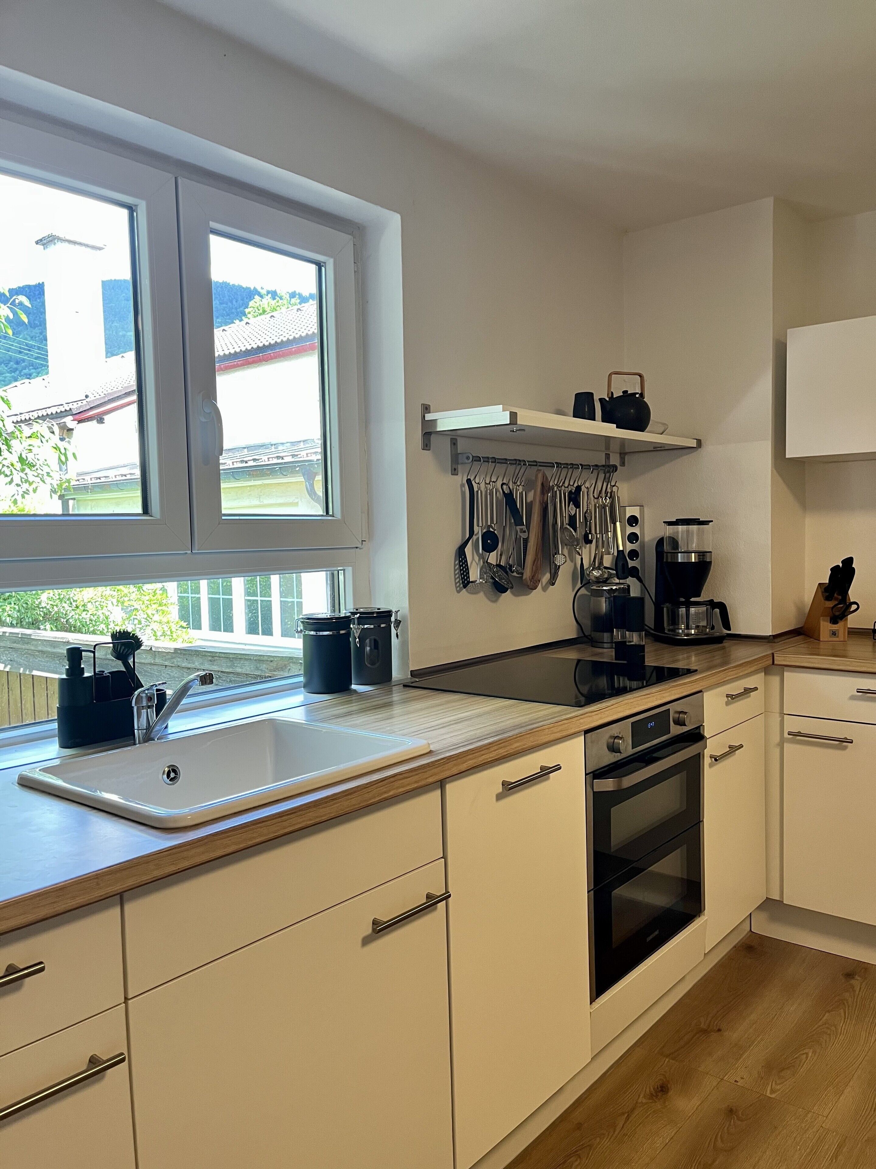 Eine moderne Küche mit einem großen Fenster, weißen Schränken, einer Holz Arbeitsplatte und Edelstahlgeräten.