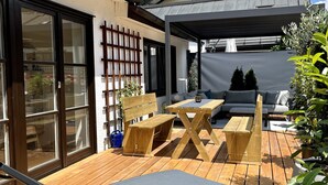 A wooden deck with outdoor furniture, including lounge chairs and a table, and a covered area with a sofa and a coffee table. - Fewo Rosenstraße (Tegernsee)