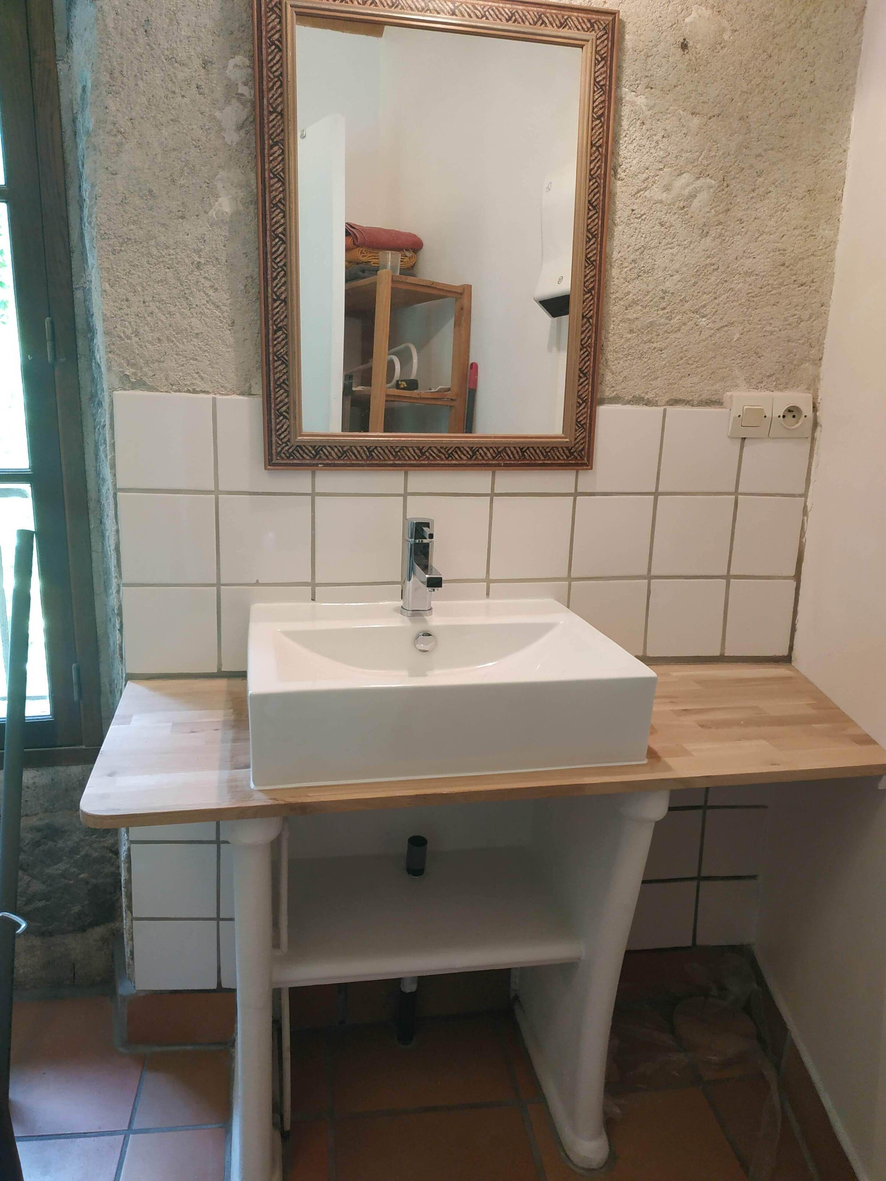 Un baño con lavamanos blanco, un espejo con marco decorativo y encimera de madera.