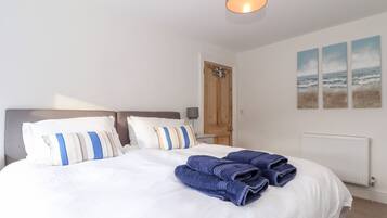 A neatly made bed with white and striped pillows, a blue towel, and a wooden door with a towel rack.