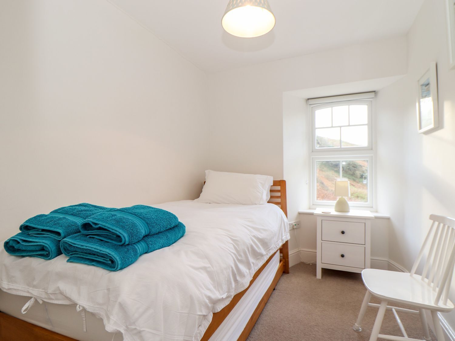 Un dormitorio con cama, mesita de noche, silla y ventana.