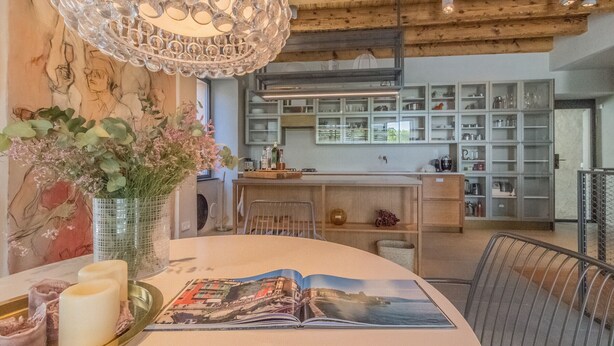 Een eetgedeelte met een tafel, stoelen, een kroonluchter en uitzicht op de keuken.