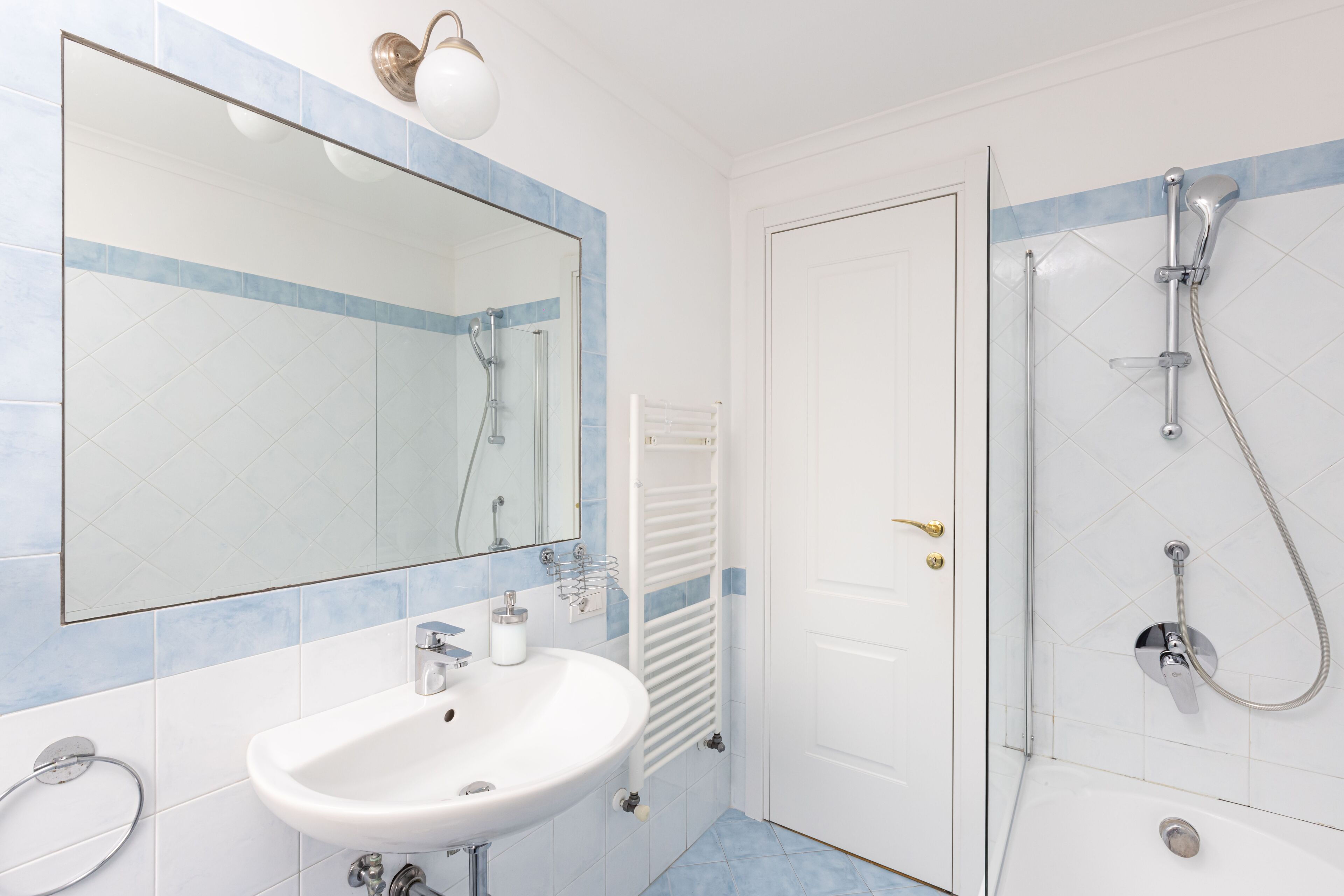 A bathroom with a white sink, a mirror, a shower, and a towel rack.