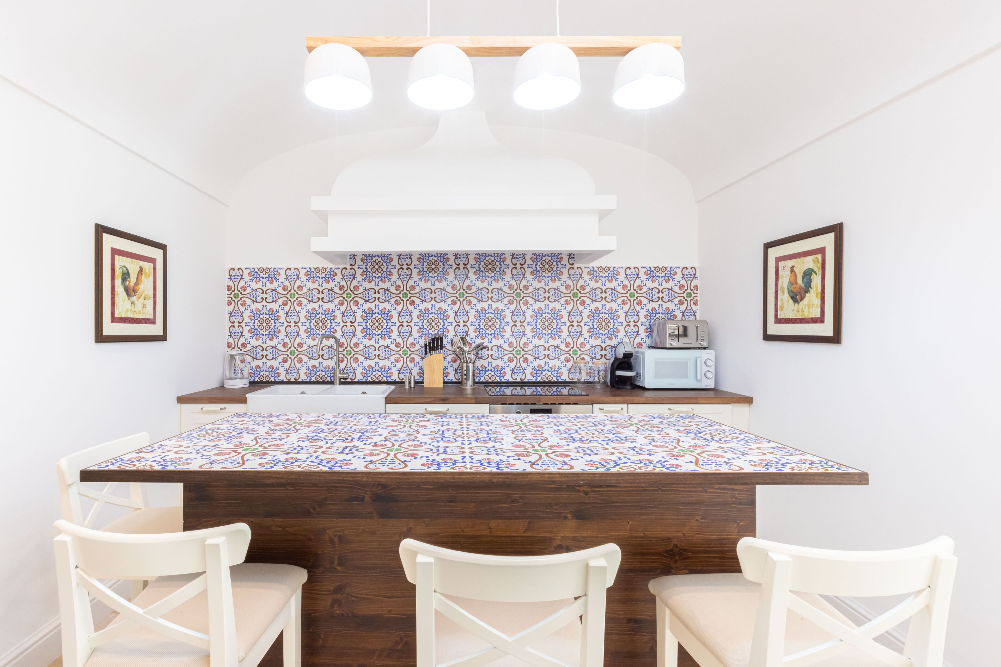 A kitchen with a tiled backsplash, a wooden island, white chairs, and a white countertop.