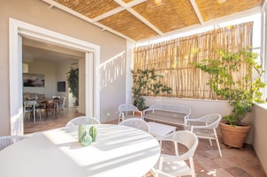 Un patio con mobiliario de mimbre blanco, una mesa con un objeto verde y una planta en maceta.
