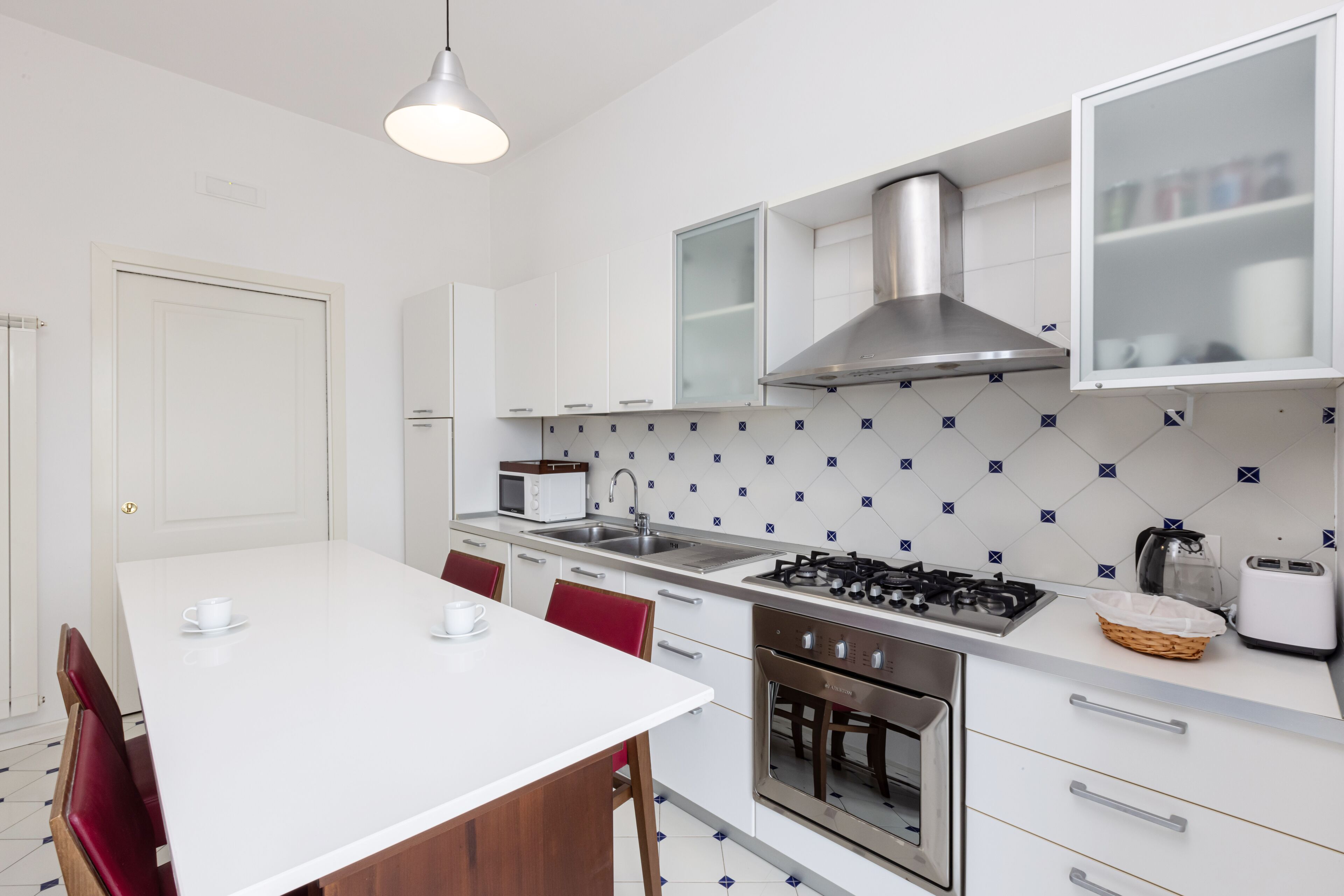 A modern kitchen with white cabinets, a stainless steel range hood, a microwave, a sink, and a gas stove.