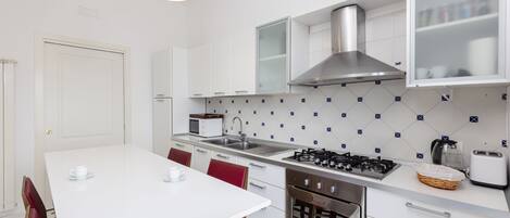 A modern kitchen with white cabinets, a stainless steel range hood, a microwave, a sink, and a gas stove.