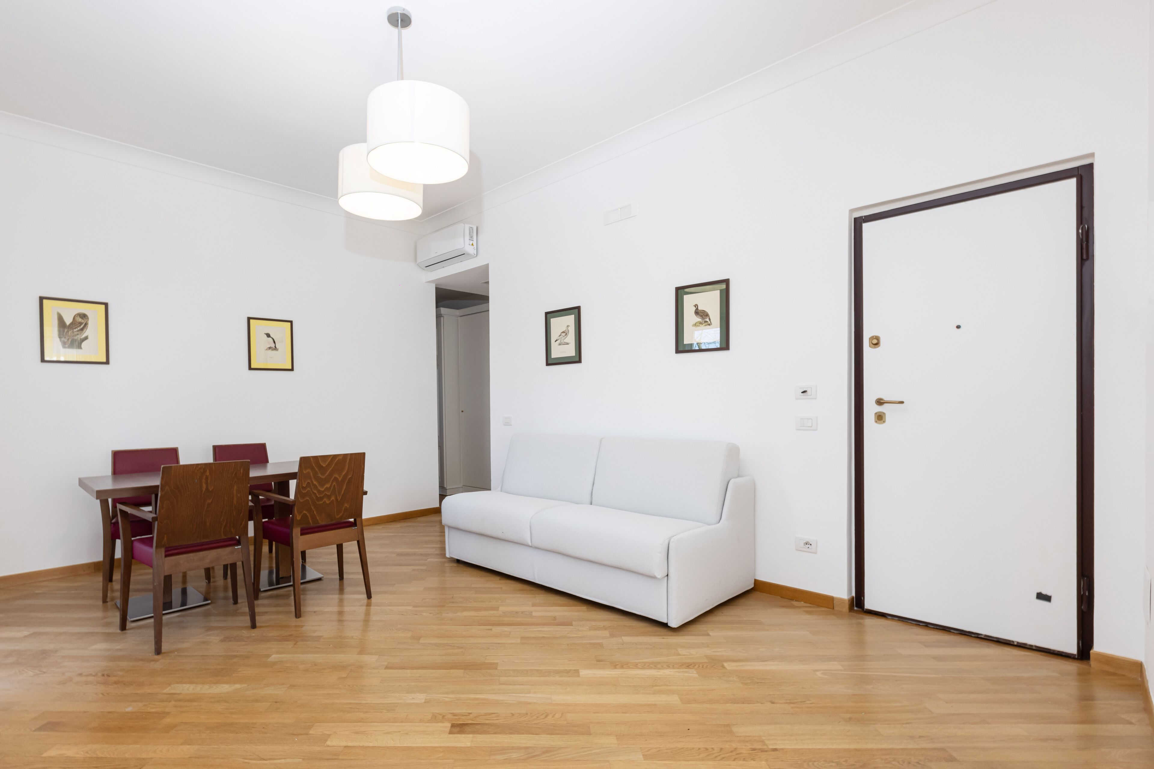 A room with a dining table, chairs, a white sofa, and a door.