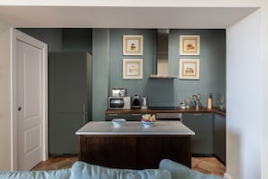 Cocina compacta con una isla central, microondas, hervidor y cuadros en la pared.