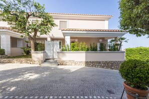 Una casa de dos pisos con techo de tejas, un muro de piedra y un camino de entrada pavimentado.
