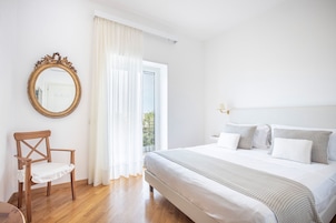 Un dormitorio con cama, una silla, un espejo y una ventana con cortinas.