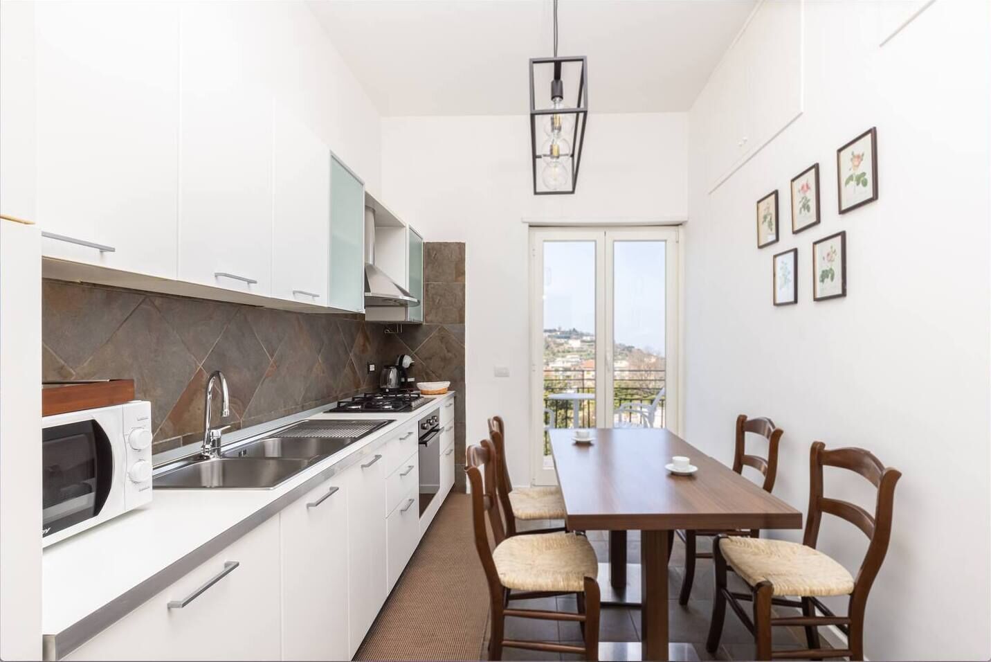 A modern kitchen with white cabinets, a built-in microwave, and a dining area with a wooden table and chairs.