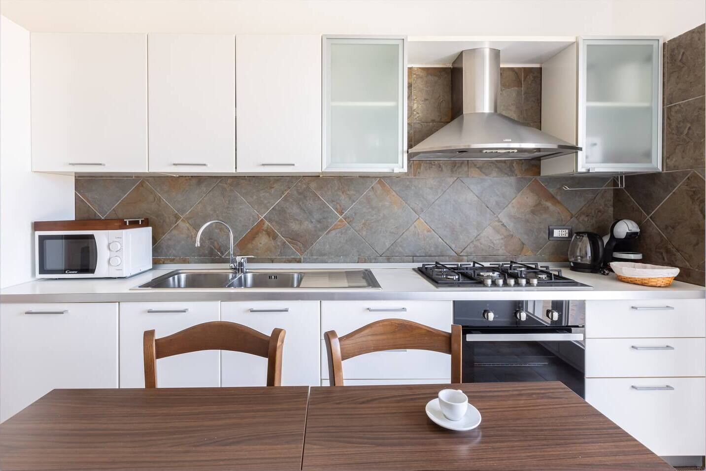 A modern kitchen with white cabinets, a microwave, a stove, and a sink.