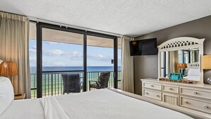 Habitación de hotel con una cama grande, un aparador, un televisor y un balcón con vista al océano.
