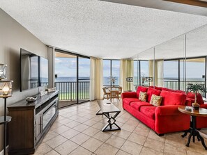 A spacious living area with a red sofa, a TV, and a balcony with a view of the sea.