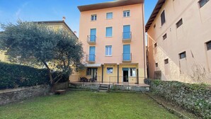 A multi-story building with balconies, a small garden area with a tree, and a stone wall. - Leonardo House Garden in Stresa Center (Stresa)