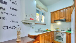 A kitchen with wooden cabinets, a white countertop, a built-in oven, and a window above the sink. - Leonardo House Garden in Stresa Center (Stresa)