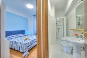 A hotel room with a bed, a shower, a sink, and a toilet.