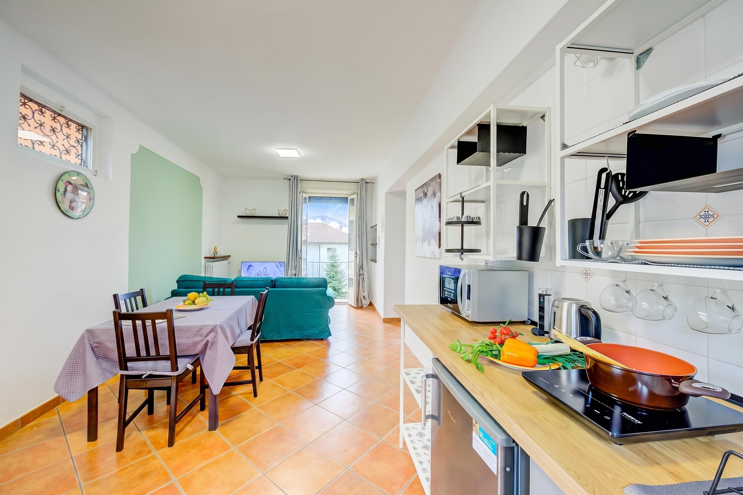 Cozinha compacta com área de refeições, um sofá verde e vista para o exterior.