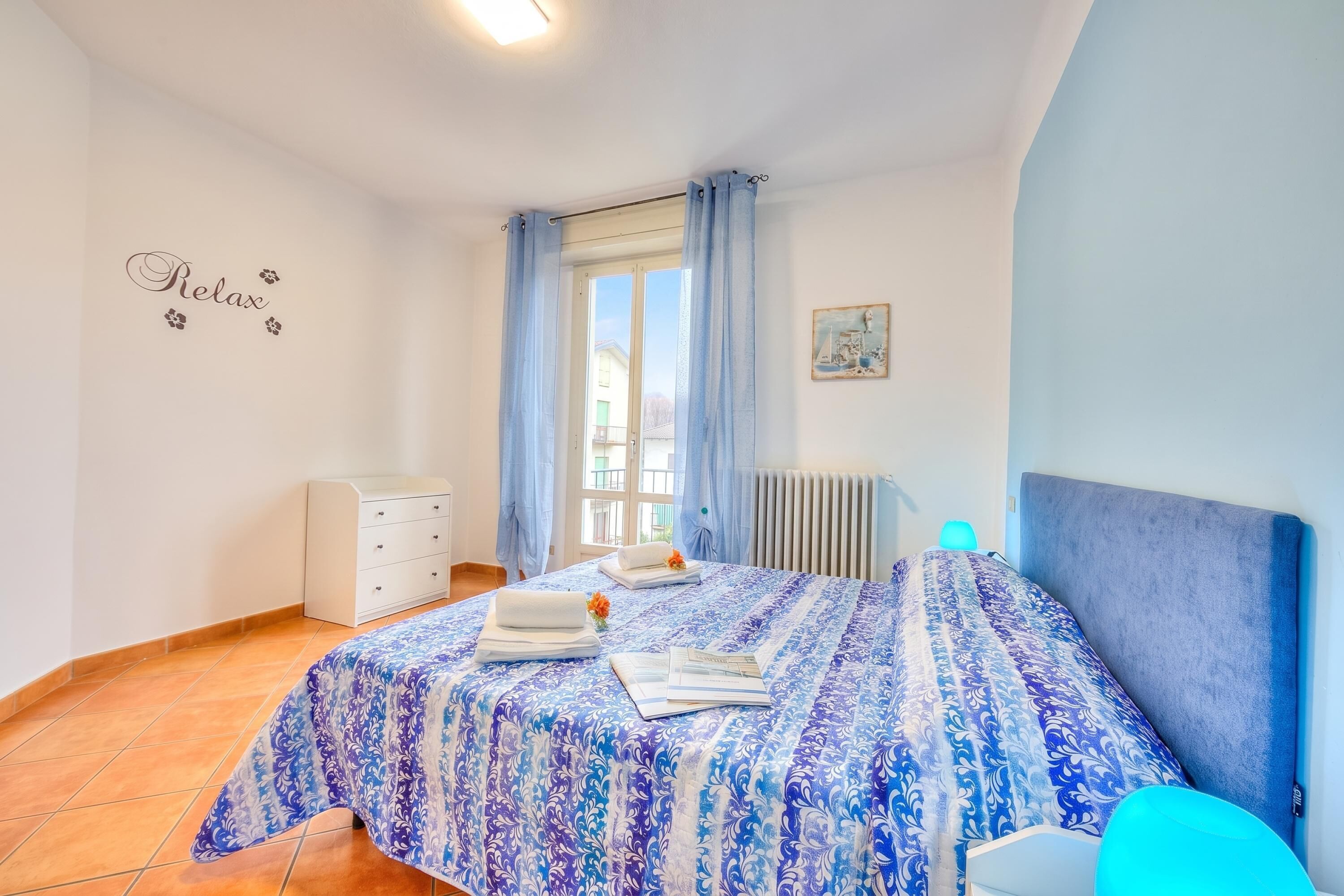 A bedroom with a bed, a dresser, a radiator, and a window with curtains.