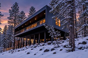 A modern two-story building with a balcony, surrounded by snow-covered trees. - Le Cabin Noir | Modern Cabin w/ Hot Tub + BBQ (Flagstaff)