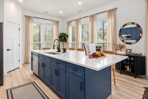 Une cuisine moderne dotée d’un îlot central, d’un four encastré et d’un coin repas avec une table et des chaises.
