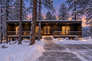 Une cabane en bois moderne dotée d’un porche abrité, entourée d’arbres couverts de neige.
