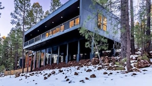 Une cabane moderne à deux étages, dotée d’un balcon et entourée d’arbres et de rochers.