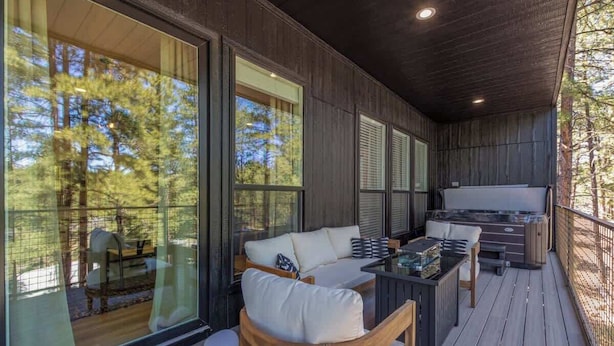 Une terrasse extérieure couverte, dotée d’un espace salon, d’un jacuzzi et de grandes fenêtres offrant une vue sur les arbres.