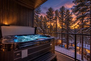 Un bain à remous sur un balcon, avec vue sur des arbres enneigés et un coucher de soleil.