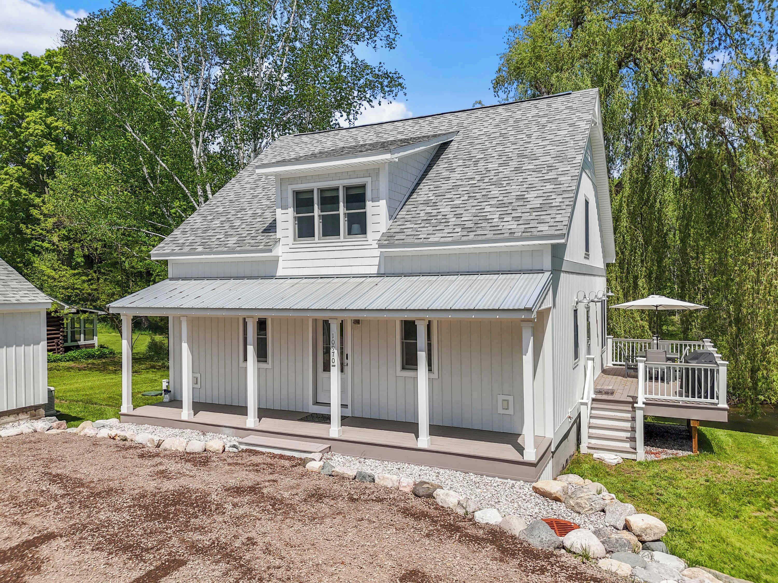 A two-story house with a covered porch, a small deck, and a pond in the background.