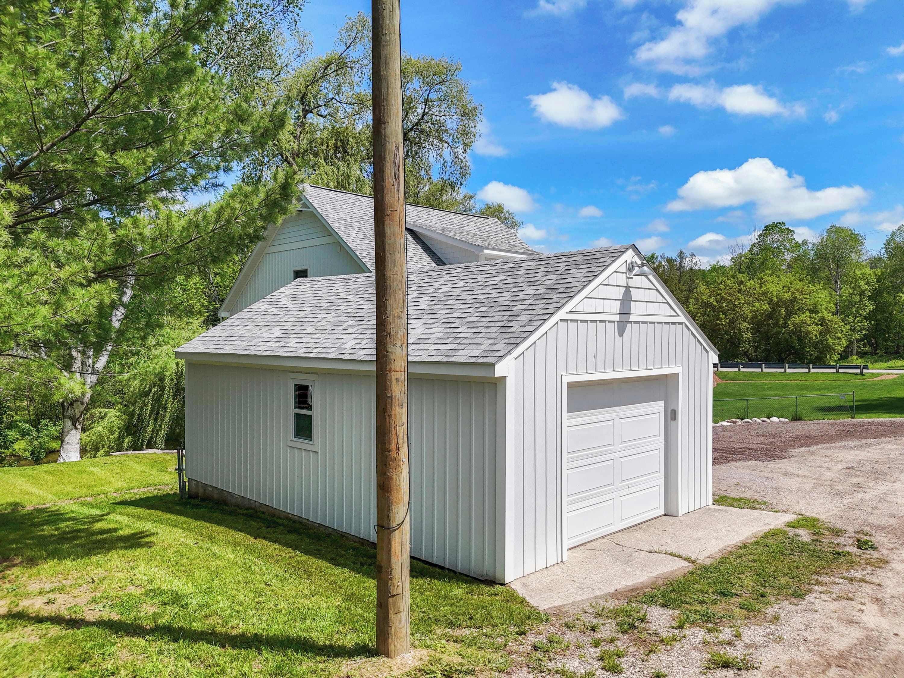 En liten, envåningsbyggnad med vit fasad och ett garage, omgiven av en gräsyta och träd.