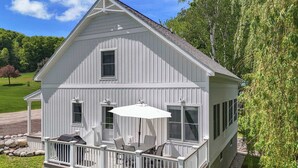 Een wit houten huis met een balkon, een overdekte patio en uitzicht op een groen landschap.