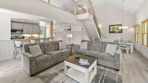 Een ruime woonkamer met een hoge plafond, een trap en een keuken op de achtergrond.