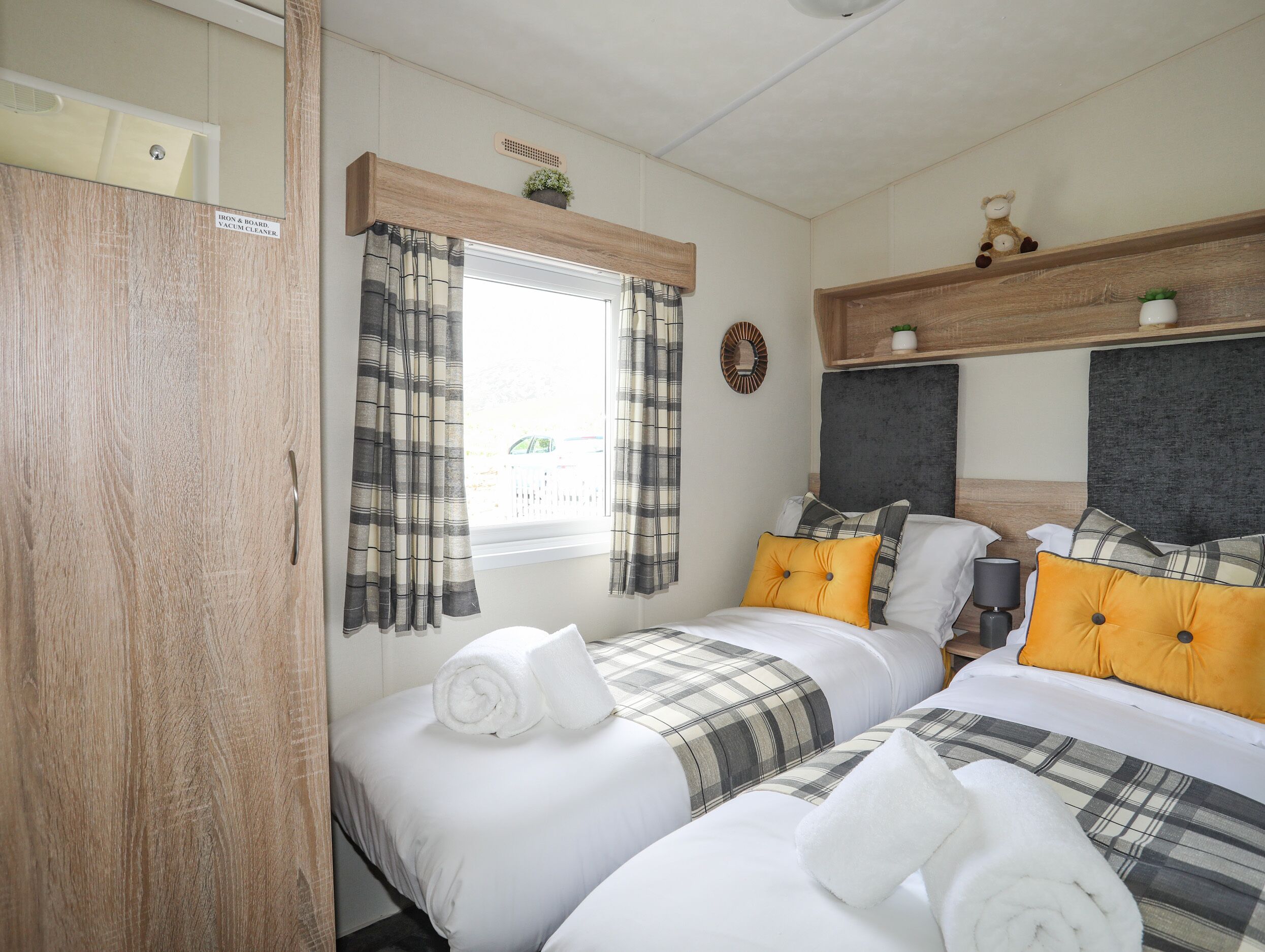 A bedroom with two beds, plaid bedding, a window with curtains, and a wooden headboard.