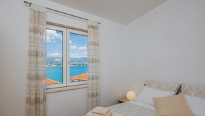 A bedroom with a bed, a window with curtains, a bedside lamp, and a view of a body of water and mountains. - Raos in Trogir - Mittel-Dalmatien / Raos in Trogir - Appartement für 4-6 Personen (Trogir)