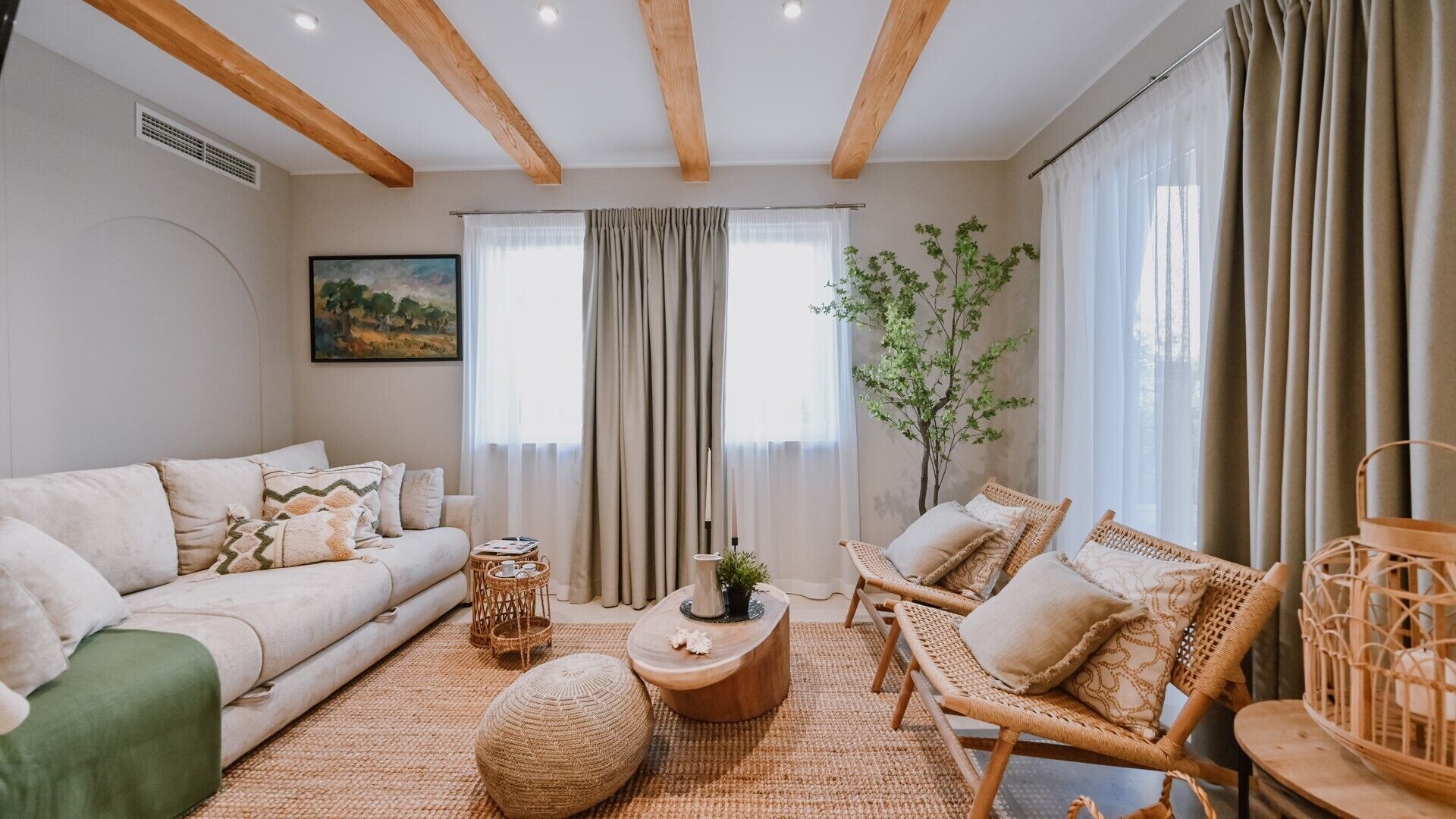 A living room with a sofa, two wicker chairs, a coffee table, and a large window with curtains.