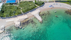Vista aérea de una zona costera con mar azul cristalino, una playa de arena y un pequeño muelle.