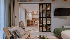 Un dormitorio moderno con una cama, una manta verde, una silla de mimbre, una mesita con una vela y un televisor montado en la pared.